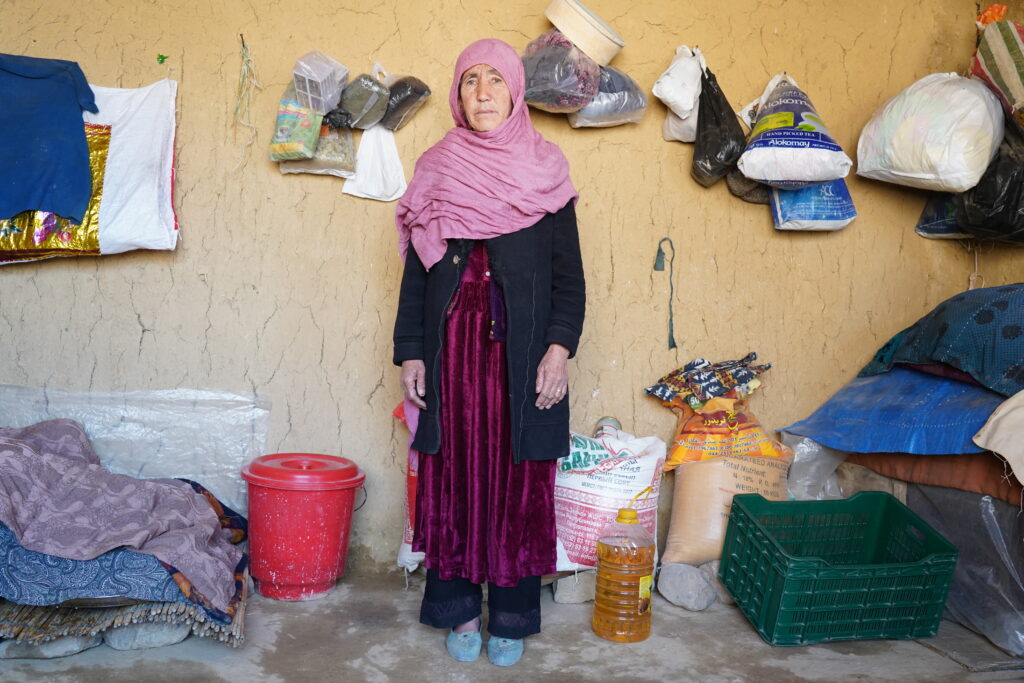 Zahra stands in her home, wearing a pink hijab and a purple dress. 